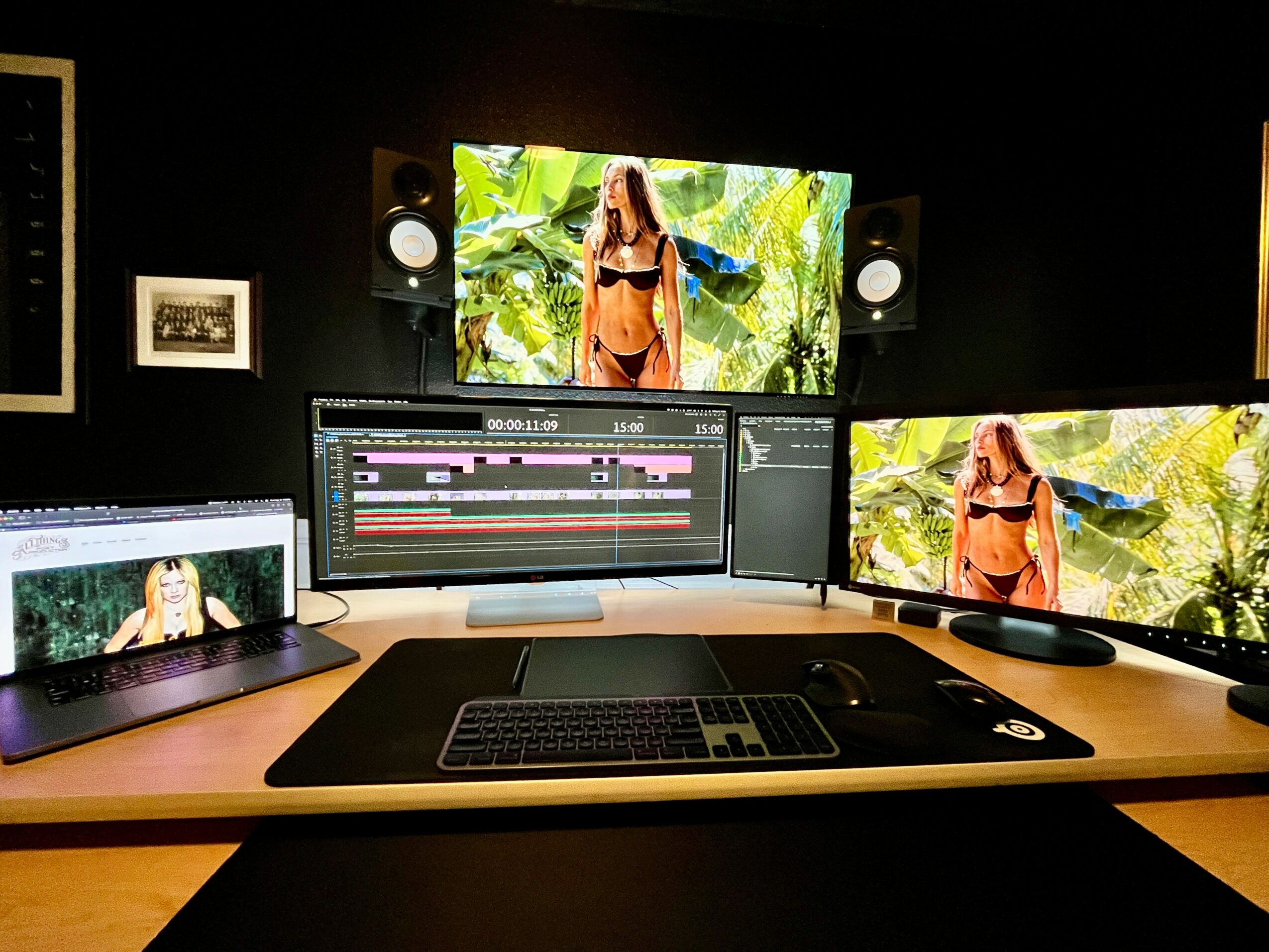 Video editing workspace with three screens displaying a woman in a jungle setting, keyboard, and editing software interface.