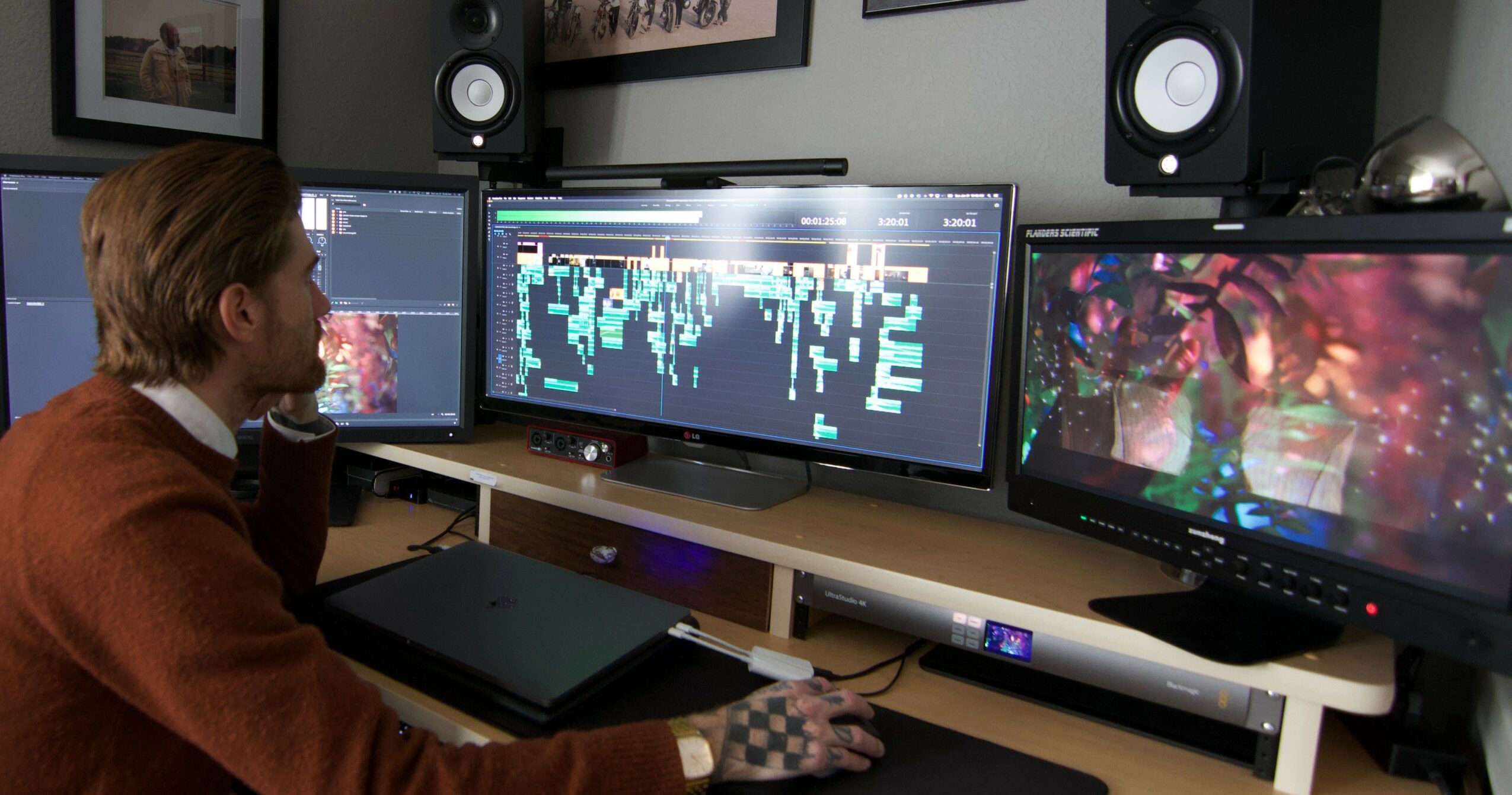 Person working at a desk with three monitors displaying digital content, in a room with speakers and framed pictures.