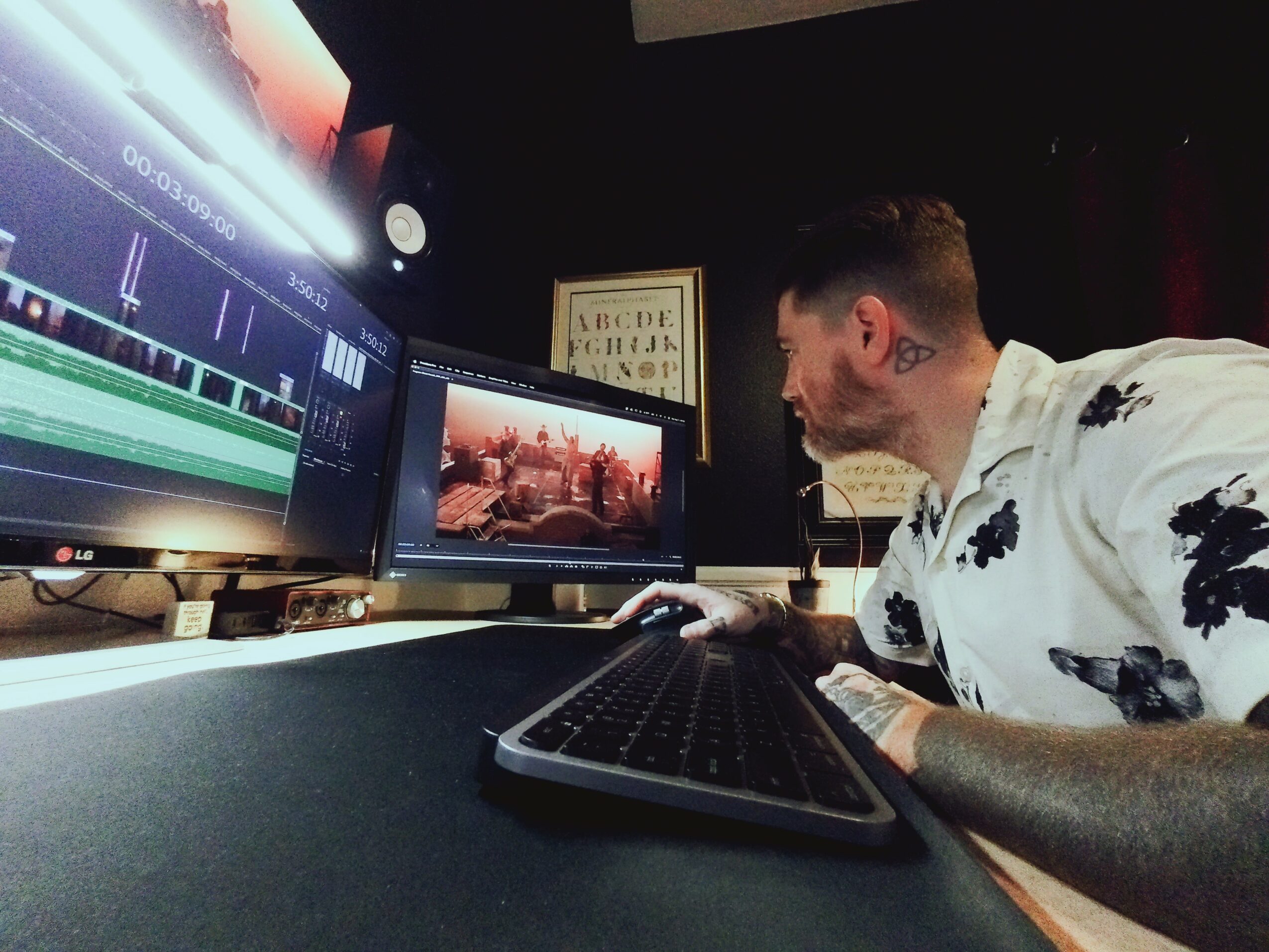 Person working at a desk with multiple monitors, one showing video editing software, in a dark room.