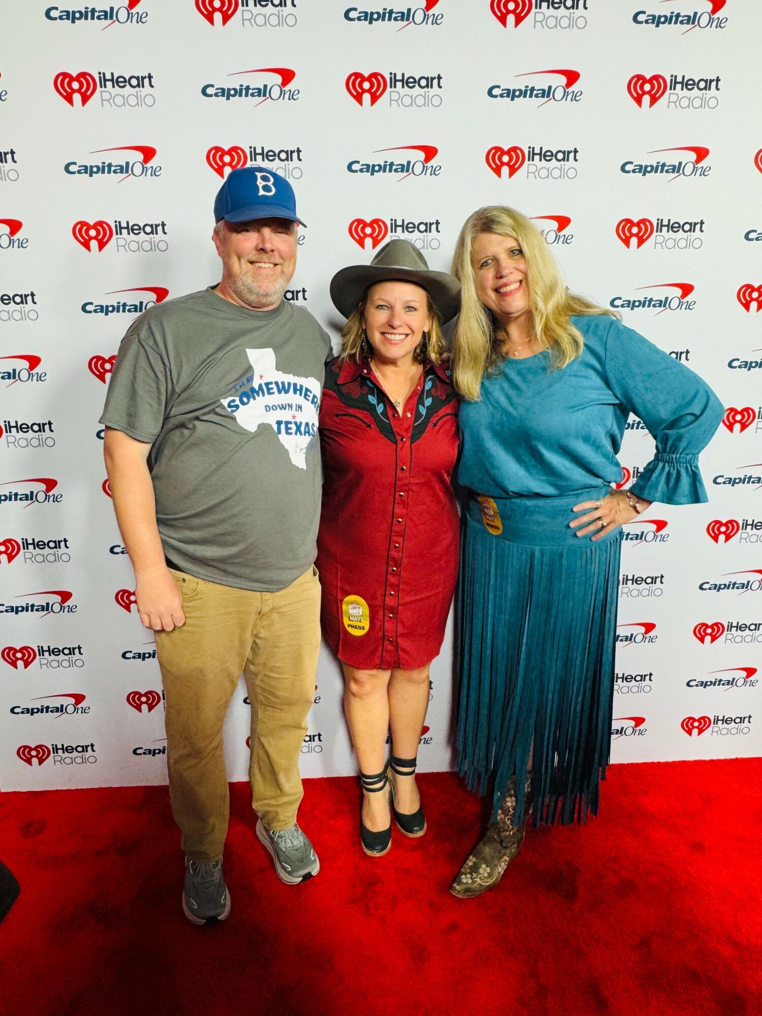 Three people standing on a red carpet in front of a backdrop with logos, smiling and posing for the photo.