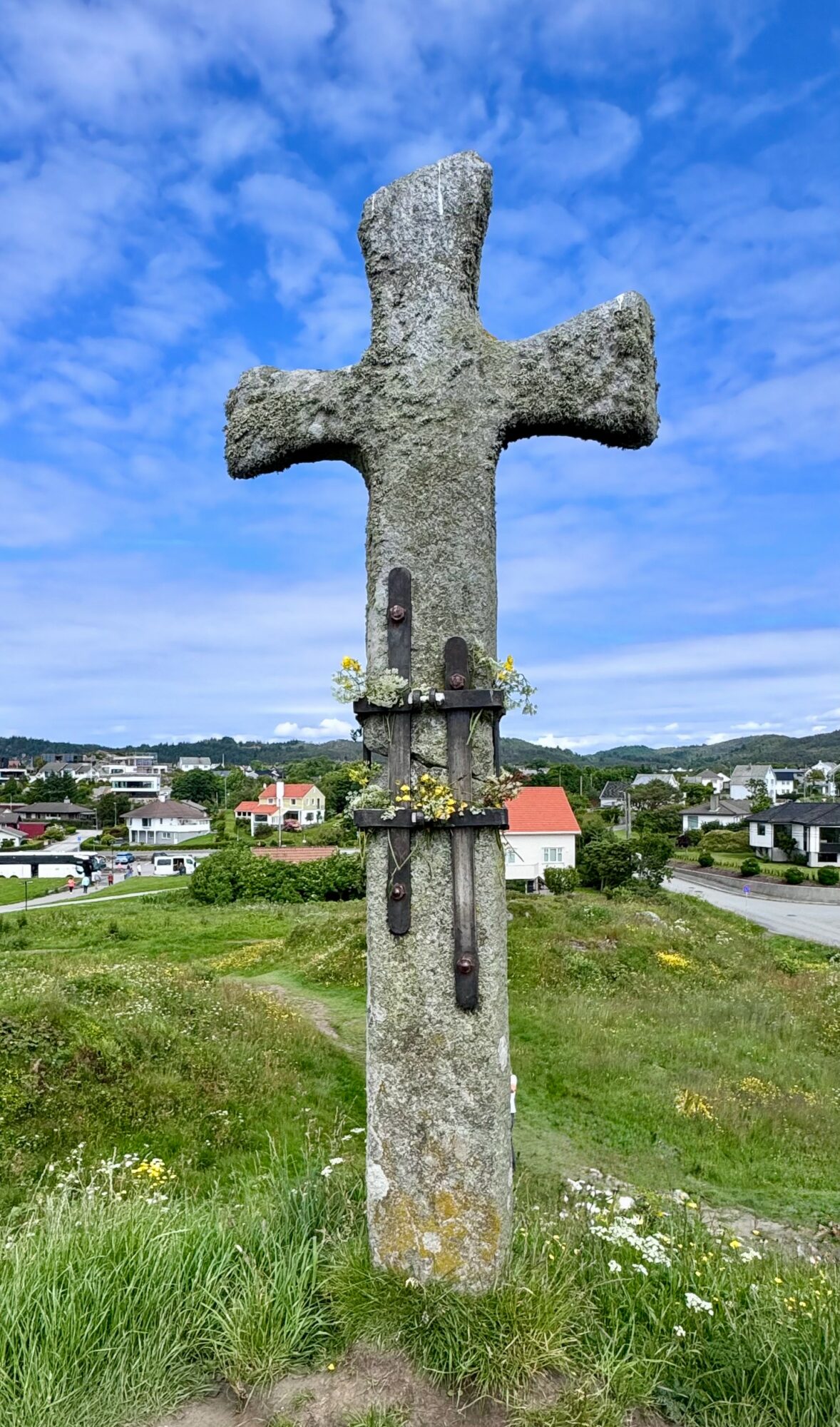 Stone cross monument with a rural landscape and blue sky in the background.