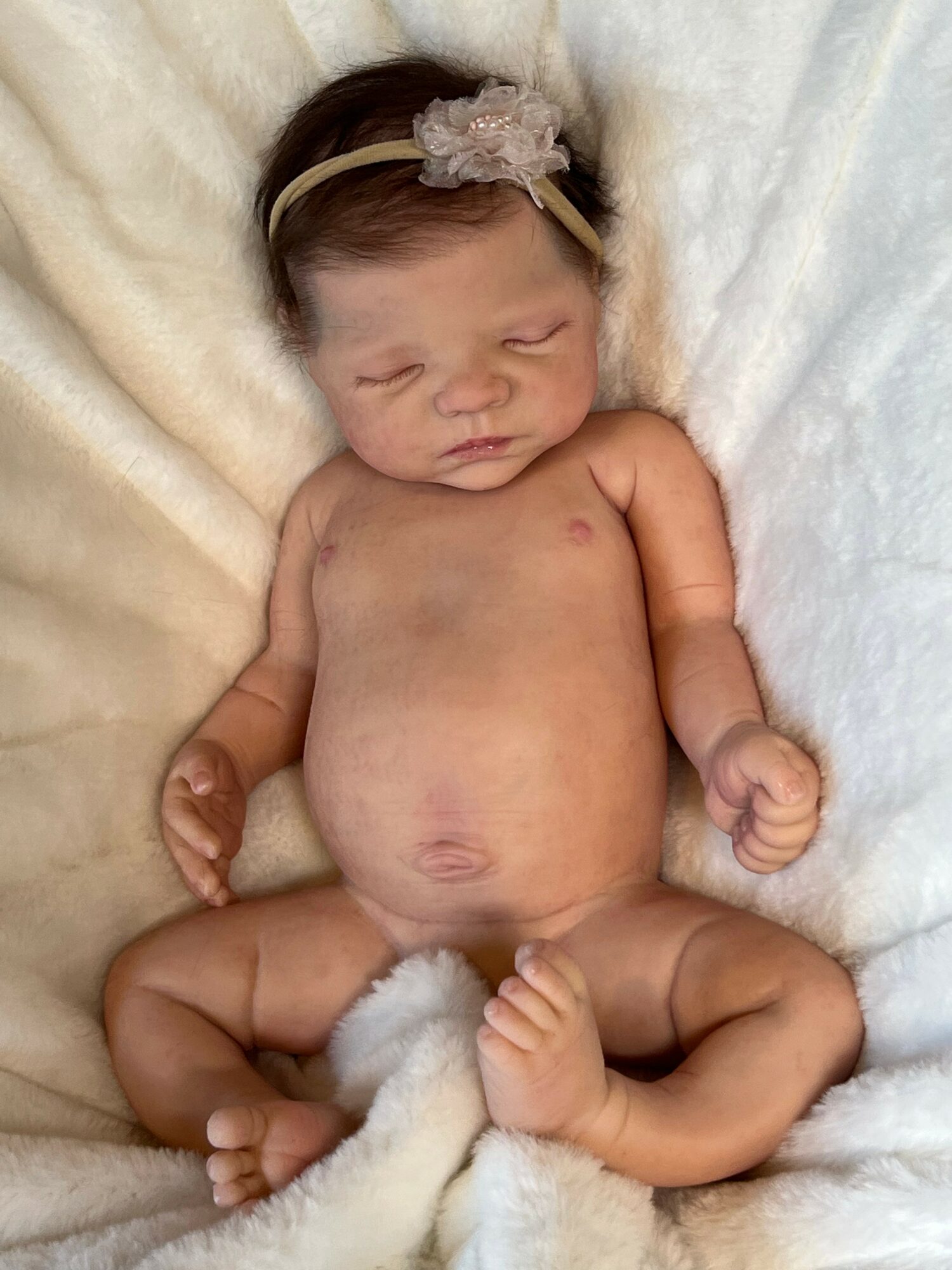 Newborn baby girl with a headband, lying on a soft blanket, eyes closed, arms and legs relaxed.