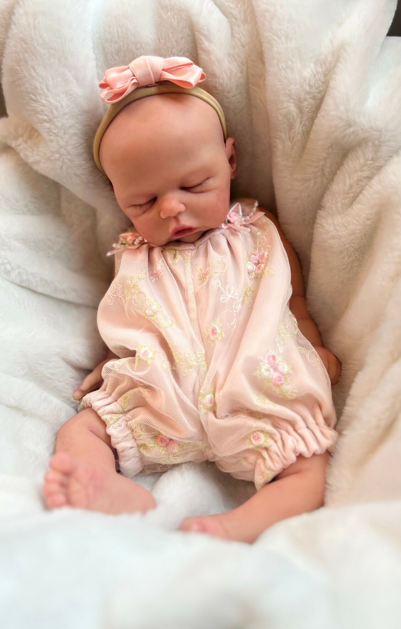 Baby girl sleeping with a pink bow headband and pastel outfit, wrapped in soft white blanket.