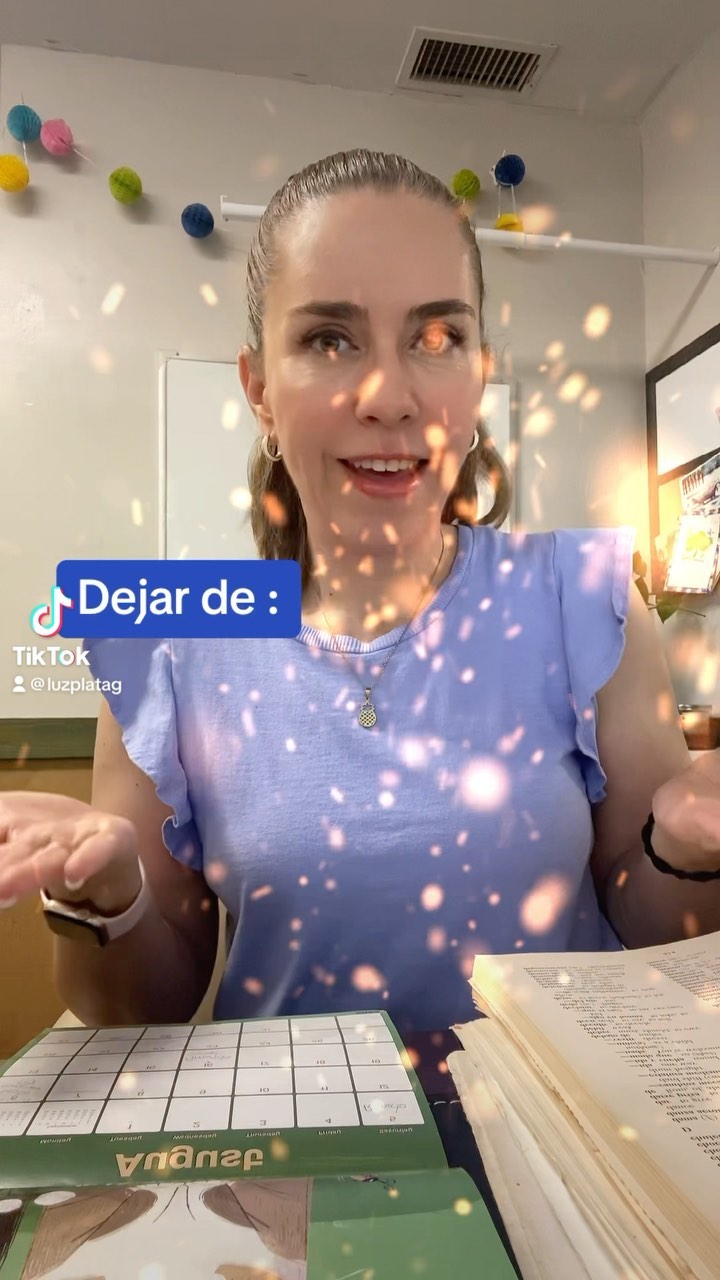 Young woman with dark hair in a ponytail, smiling, wearing a blue top, surrounded by sparkles, in a room with decorations and books.