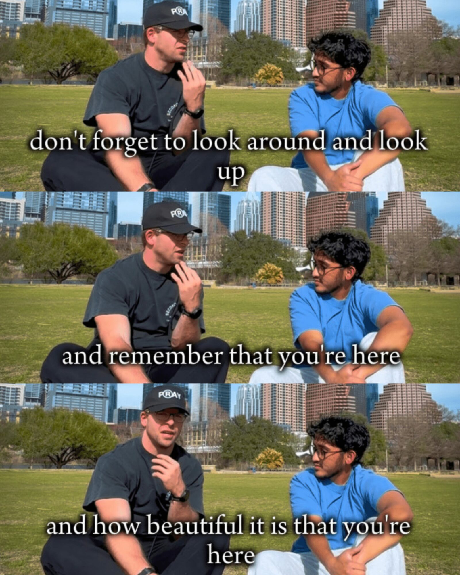 Two men sitting outdoors in a park with city buildings in the background, engaged in conversation. One man is wearing a black cap and shirt, the other a blue shirt. Subtitles display dialogue about looking around and appreciating beauty.