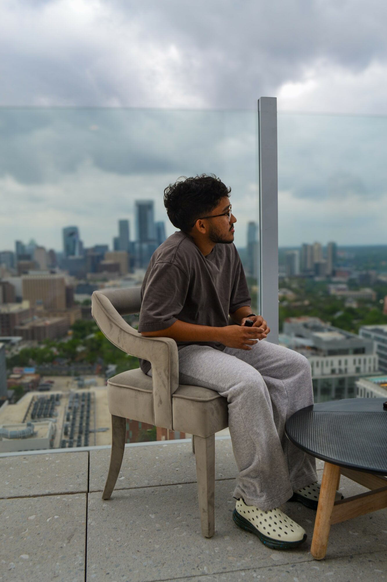 Person sitting on a chair on a rooftop with a city skyline in the background, cloudy sky overhead.
