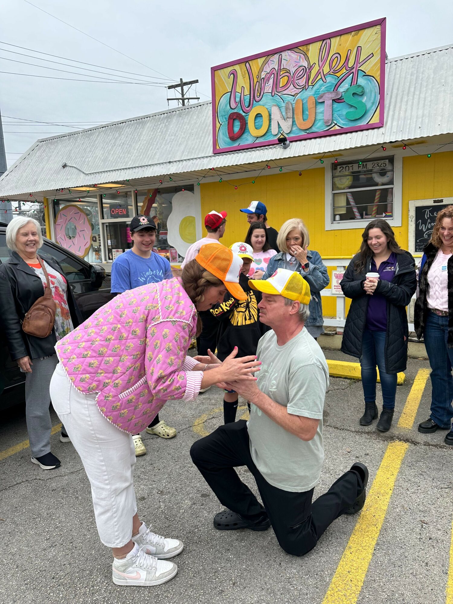 Group of people gathered outside a building with a colorful sign that reads 'Welcome Donuts'.