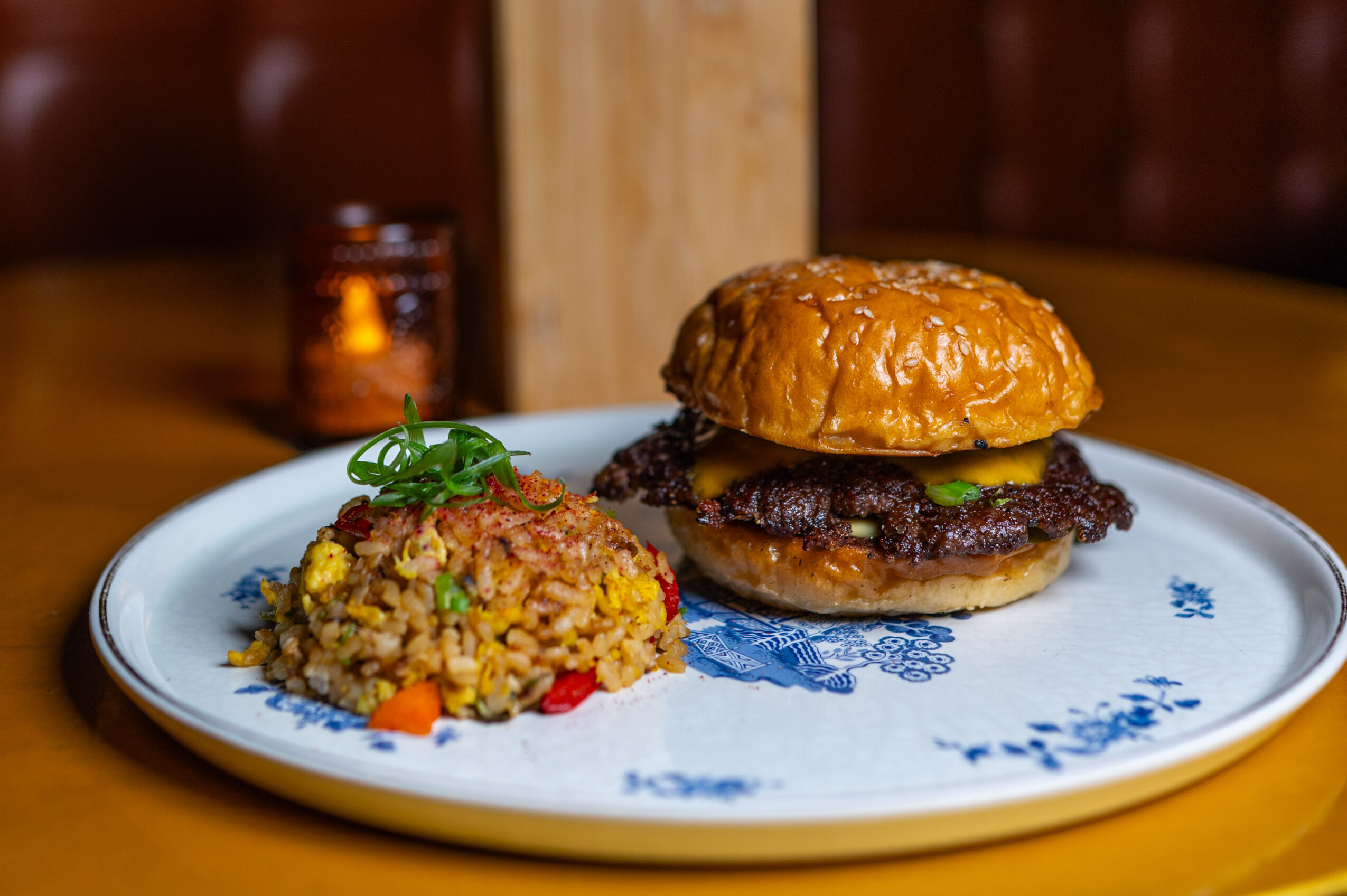 Burger with beef patty, cheese, and bun, served with fried rice on a white plate, on a wooden table.