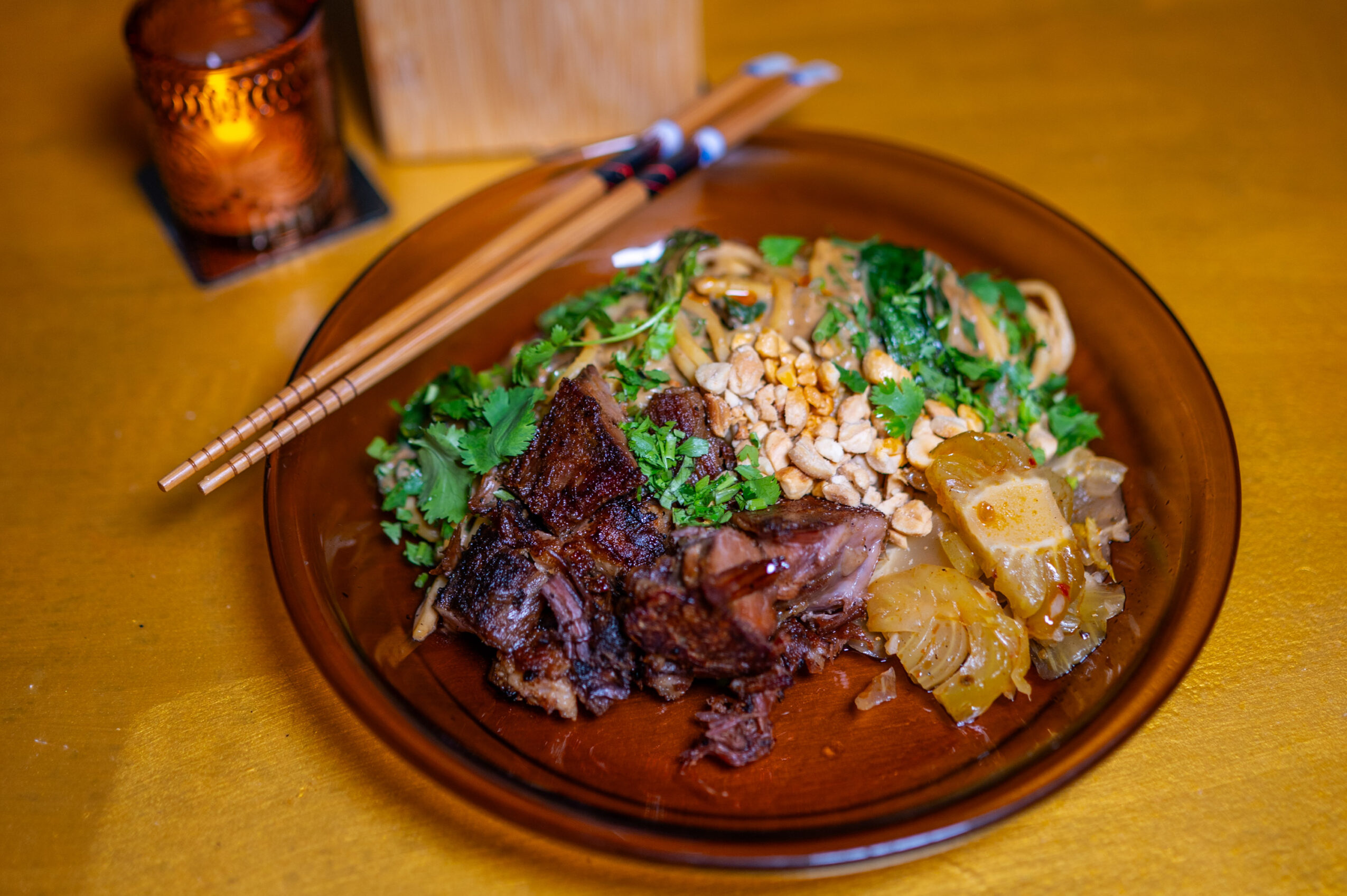 A plate with rice, meat, and vegetables on a wooden table, with chopsticks resting on the plate's edge.