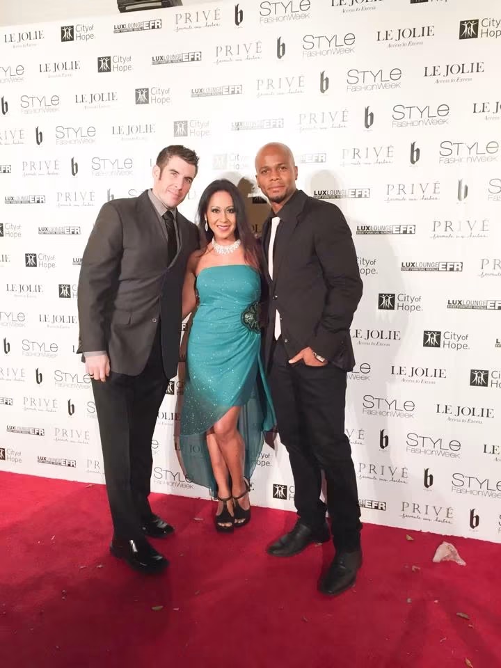 Three people standing on a red carpet in front of a step-and-repeat backdrop, smiling for the photo.