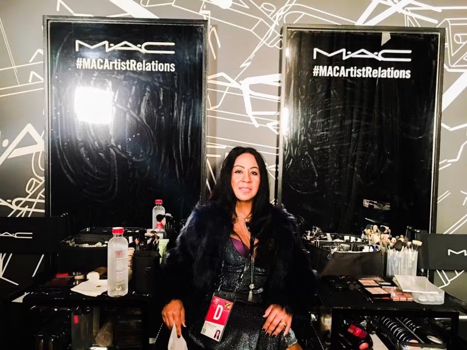 Woman with dark hair and black coat standing in front of MAC display at event.