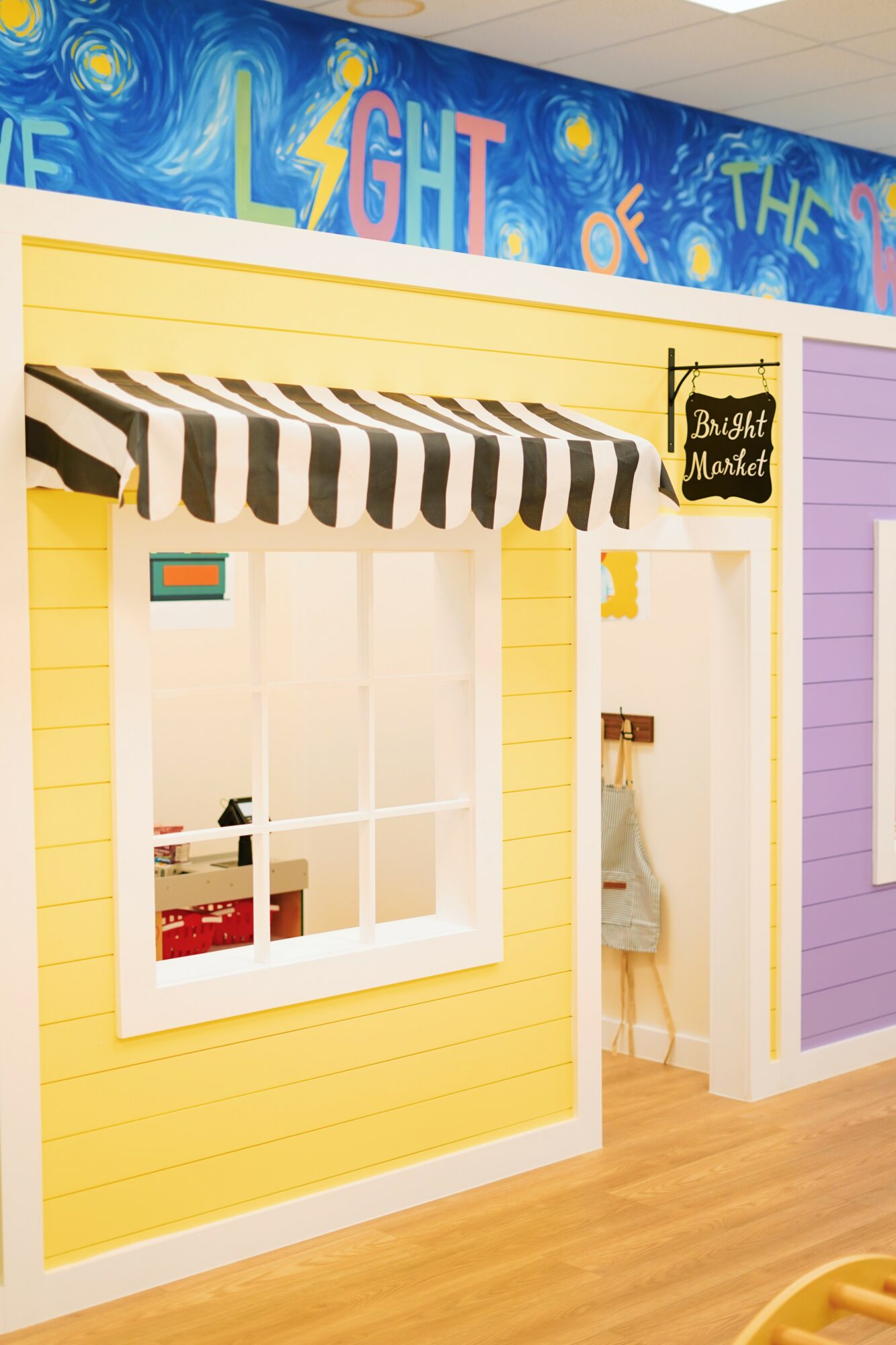 Colorful storefront with striped awning, window, and a small chalkboard sign, inside a vibrant, decorated space.