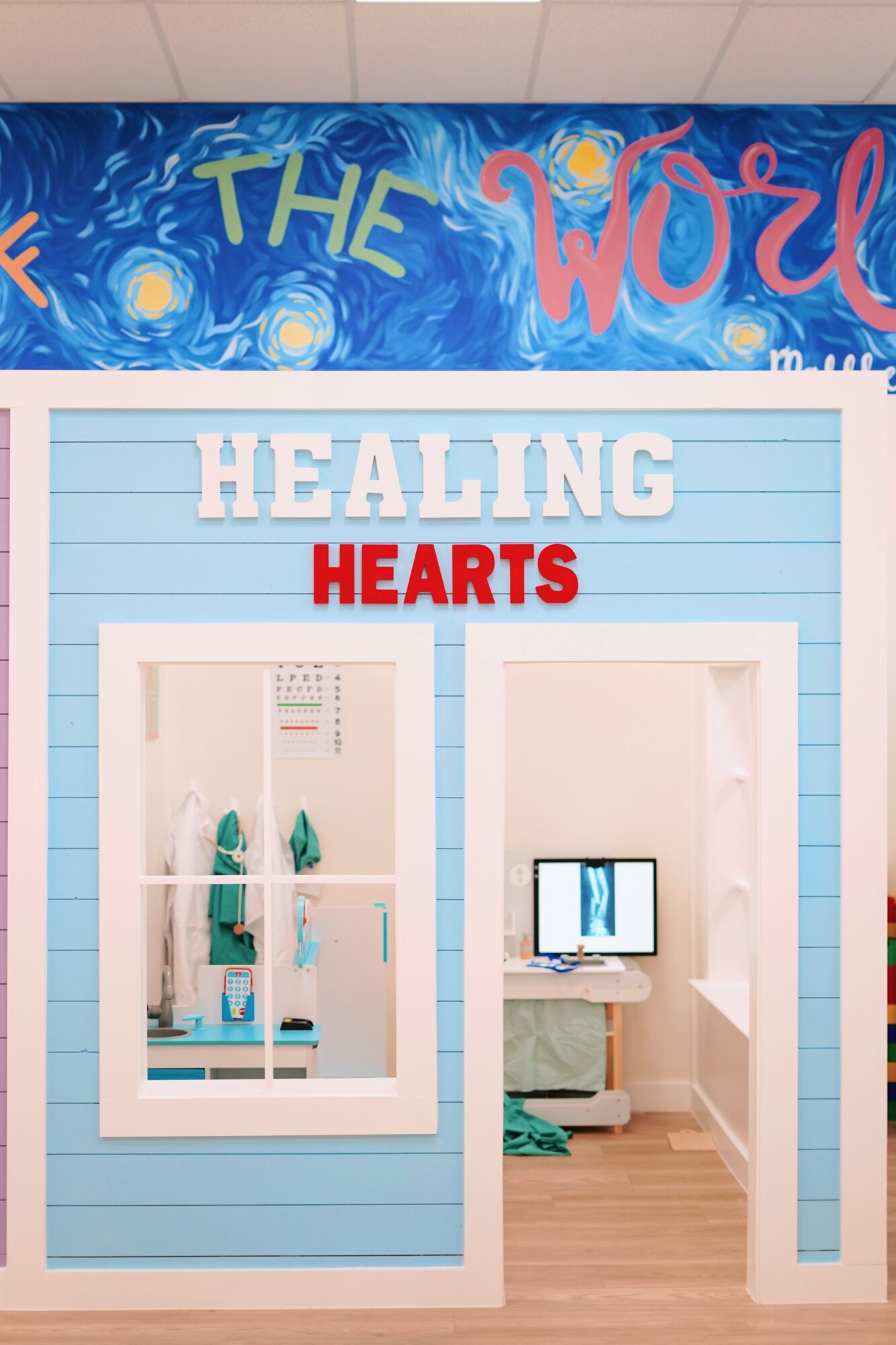 View of a room with a window showing a coat rack and a computer on a desk, blue walls, and wooden floor.