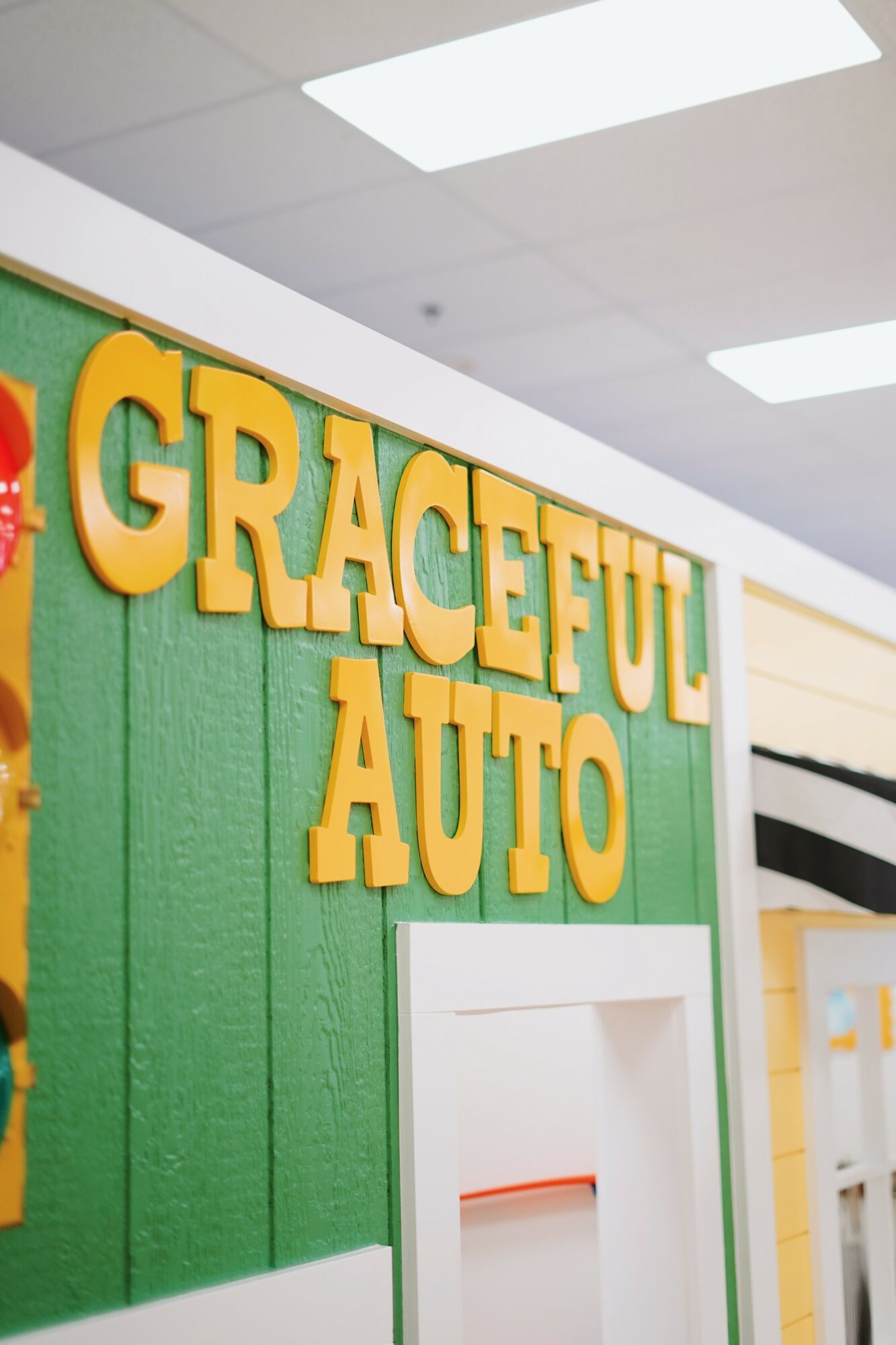 Sign with yellow letters reading 'GRACEFUL AUTO' on a green wall, part of an indoor setting.