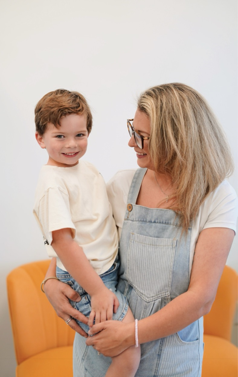 Woman holding a smiling young boy, both looking at each other, against a plain white background.