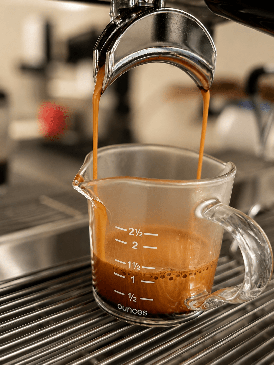 Coffee flows from a faucet into a glass measuring cup on a kitchen sink, with a blurred background.