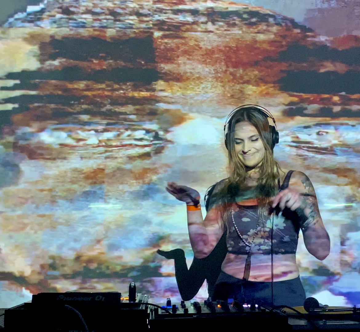 Female DJ wearing headphones, smiling, with colorful abstract background, operating DJ equipment.