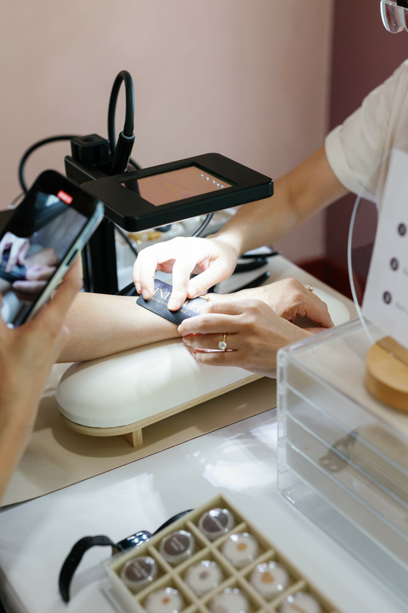 Person receiving a manicure at a salon, with a technician applying polish, and a person taking a photo.