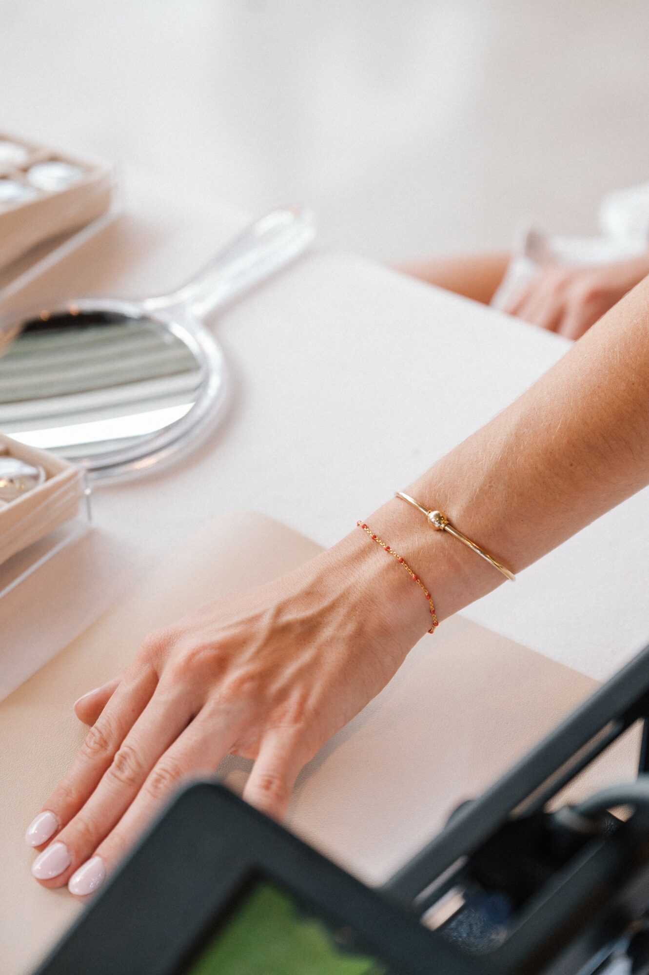 Close-up of a person's hand and wrist with jewelry, resting on a white surface, with medical tools nearby.