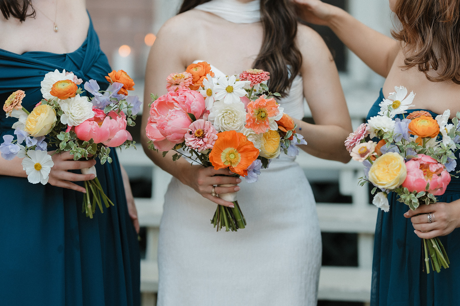 Three women holding colorful bouquets of flowers, wearing dresses, with a blurred outdoor background.