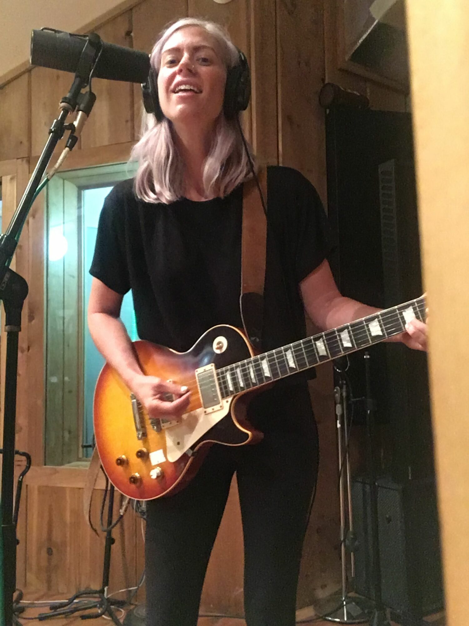 Person holding a sunburst electric guitar in a room with wooden walls and a microphone stand.