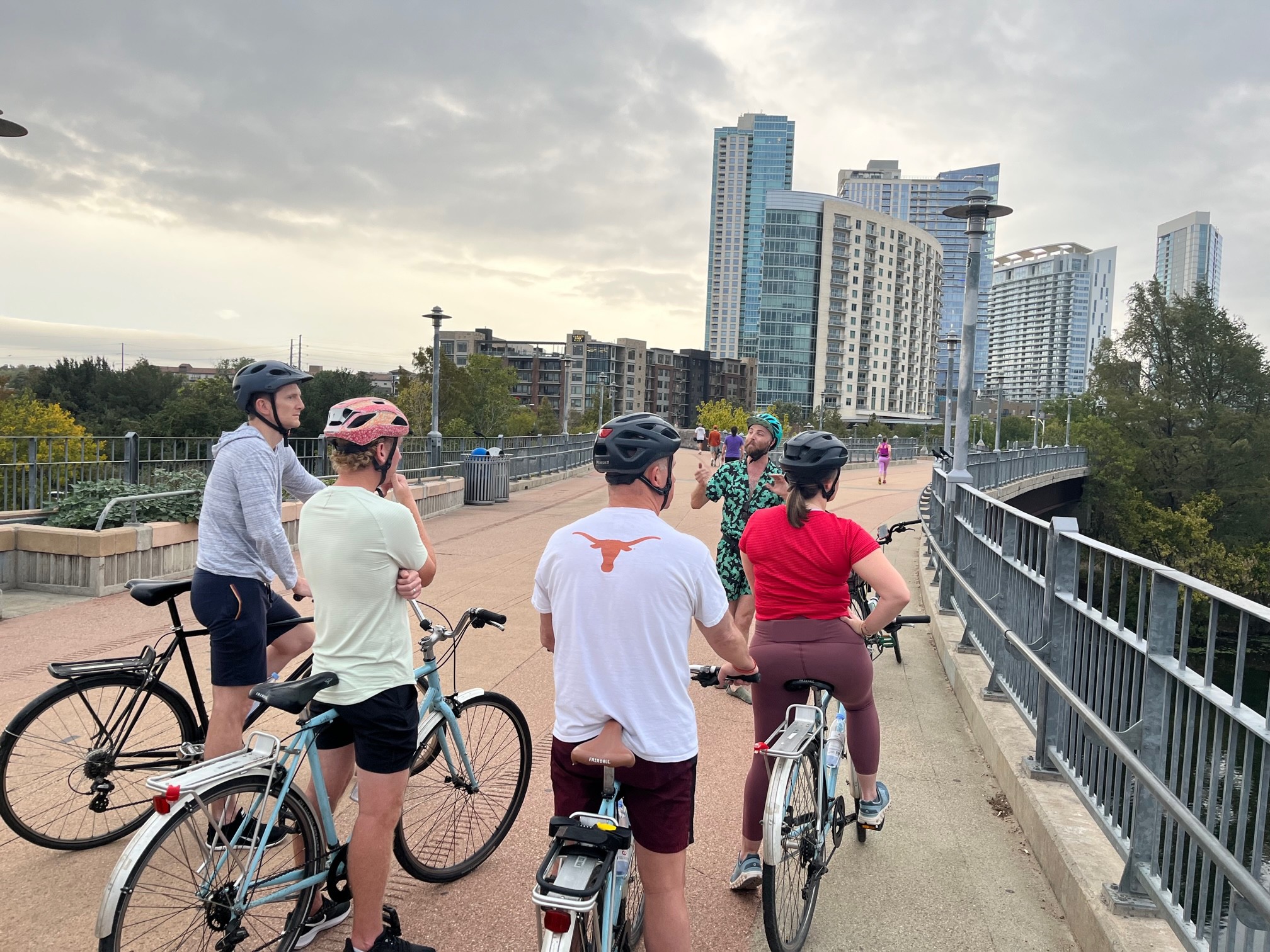 Group of people with bicycles walking on a bridge with city buildings in the background.