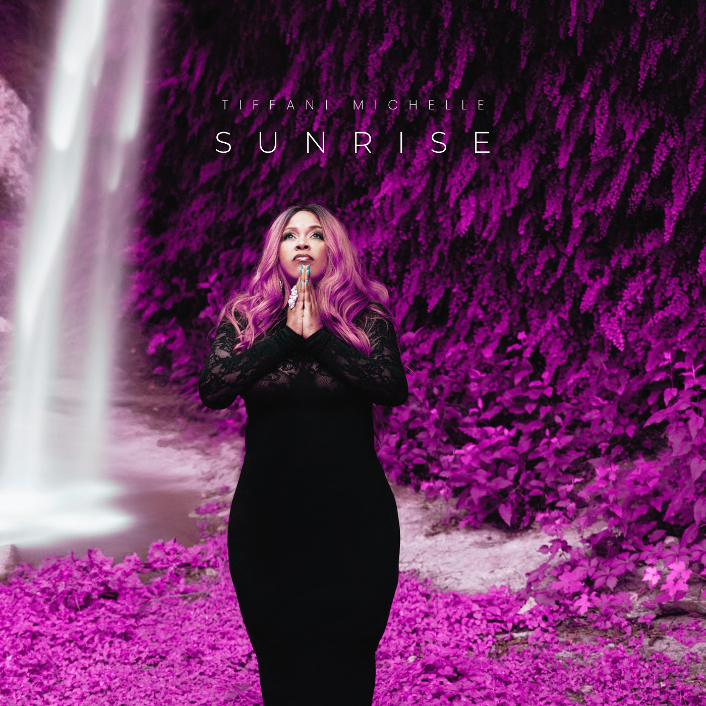 Woman with pink hair in a black dress praying in front of a purple floral background with a waterfall.
