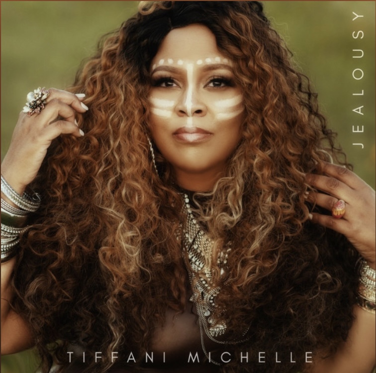Woman with curly hair and jewelry, looking at camera outdoors, with text 'JEA LOUSY' and 'TIFFANI MICHELLE'.