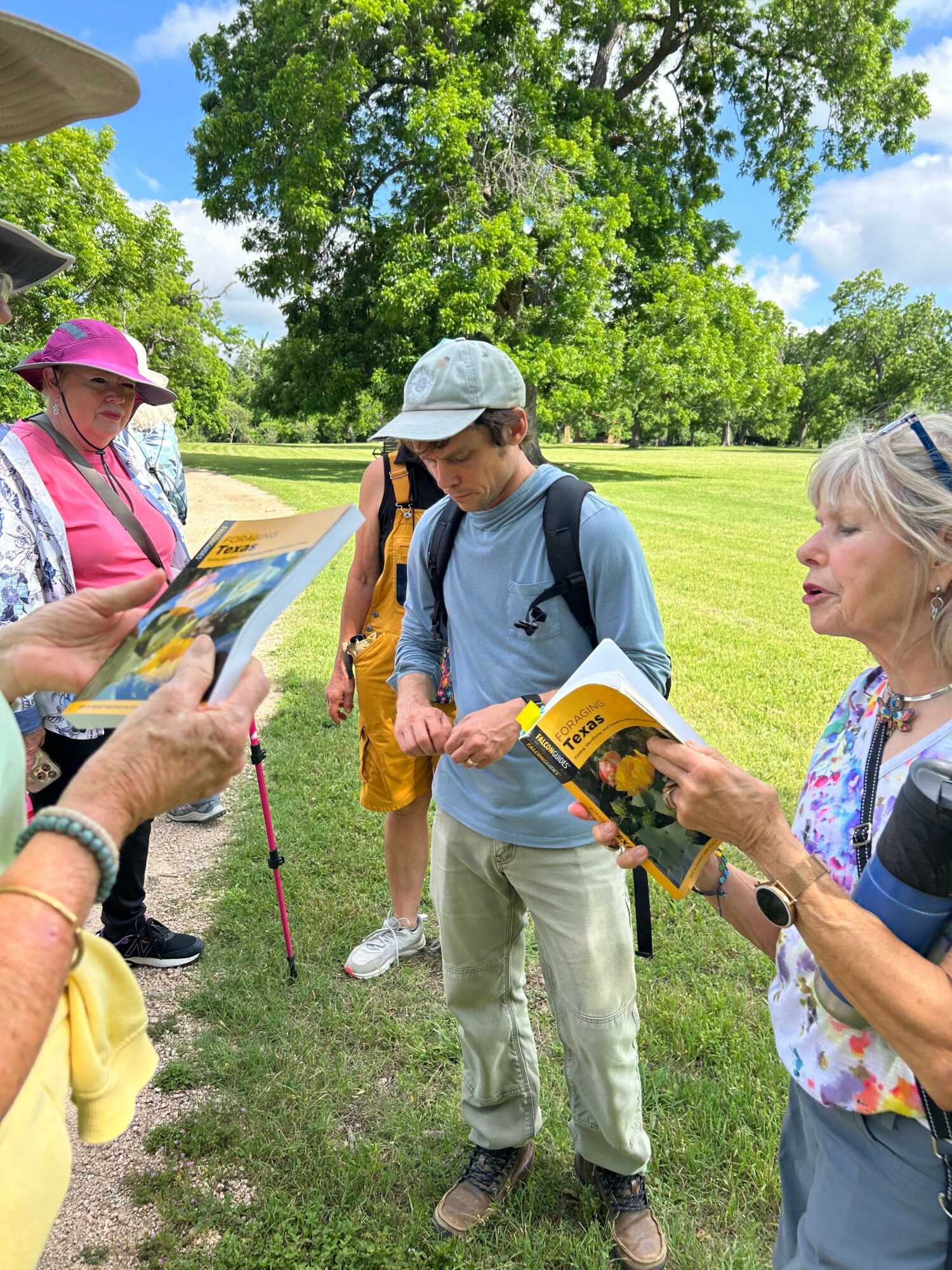 Two women and a man outdoors, looking at a map, with trees and grass in the background.