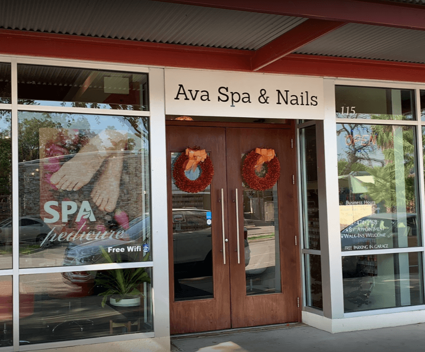 Storefront with sign 'Ava Spa & Nails' and wooden door decorated with two wreaths, glass windows on sides, and reflections outside.