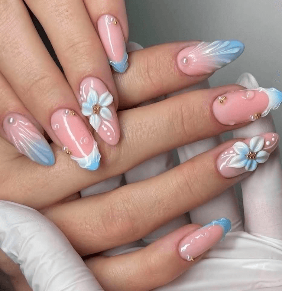 Close-up of hands with decorated nails featuring pink, blue, and white floral designs and small embellishments.