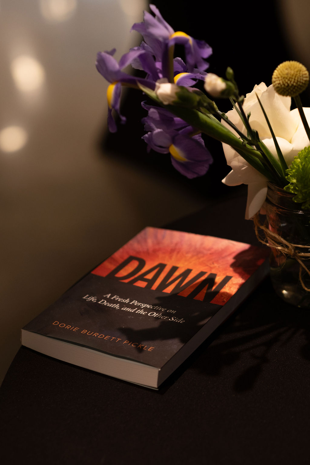 Book titled 'Dawn' on a dark surface with a bouquet of purple and white flowers nearby.