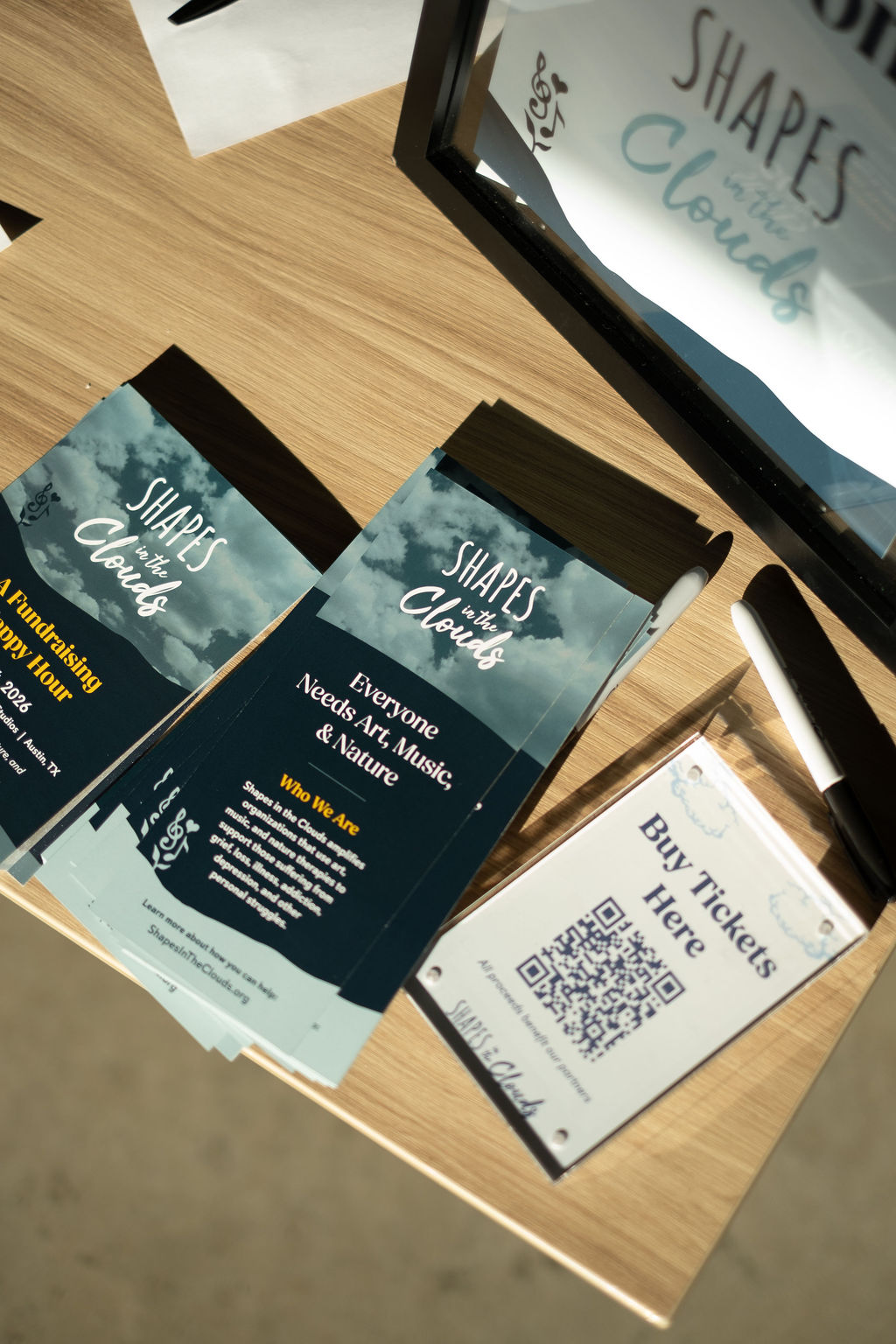 Brochures and tickets on a wooden table, with a monitor displaying text about shapes and clouds.