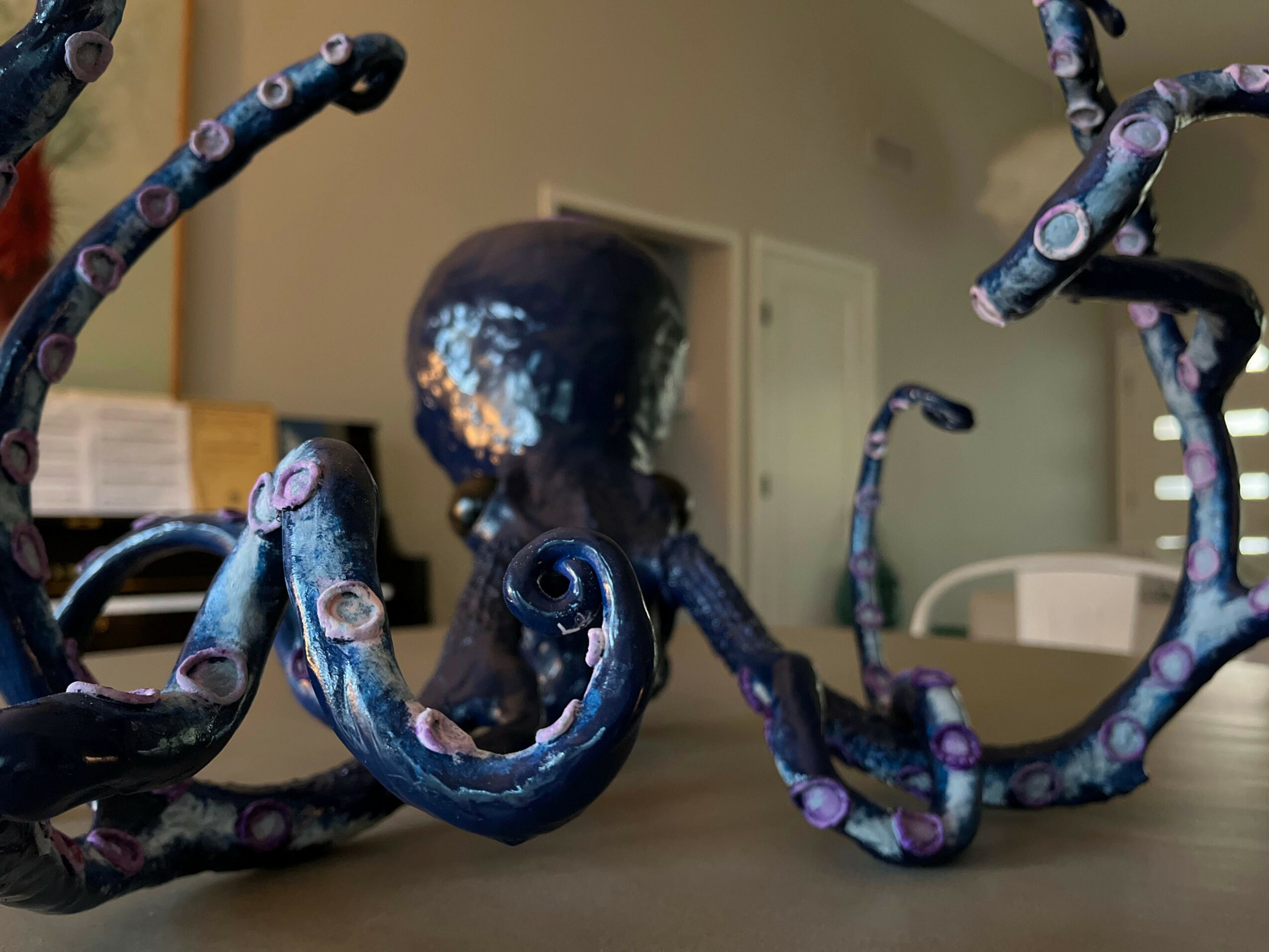Close-up of a colorful octopus sculpture with tentacles spread out on a table, background shows a room with a door and furniture.
