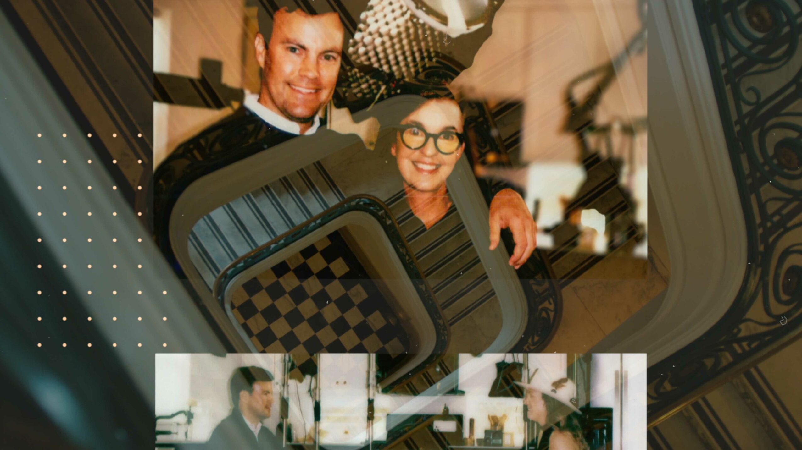 Two people smiling, holding a checkered object, standing indoors near a window with decorative ironwork.
