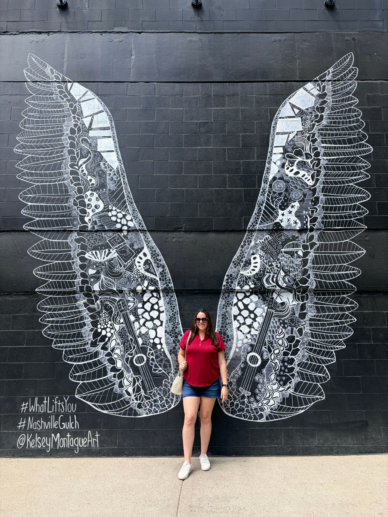 Person in red shirt and shorts standing in front of a large butterfly illustration on a black wall, with reflection below.