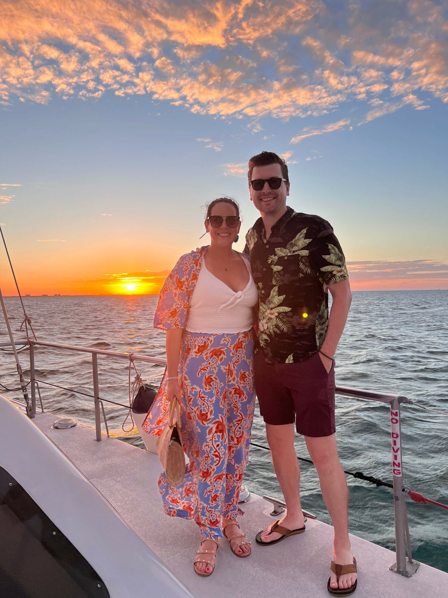 Two women stand on a boat at sunset with the ocean and sky in the background.