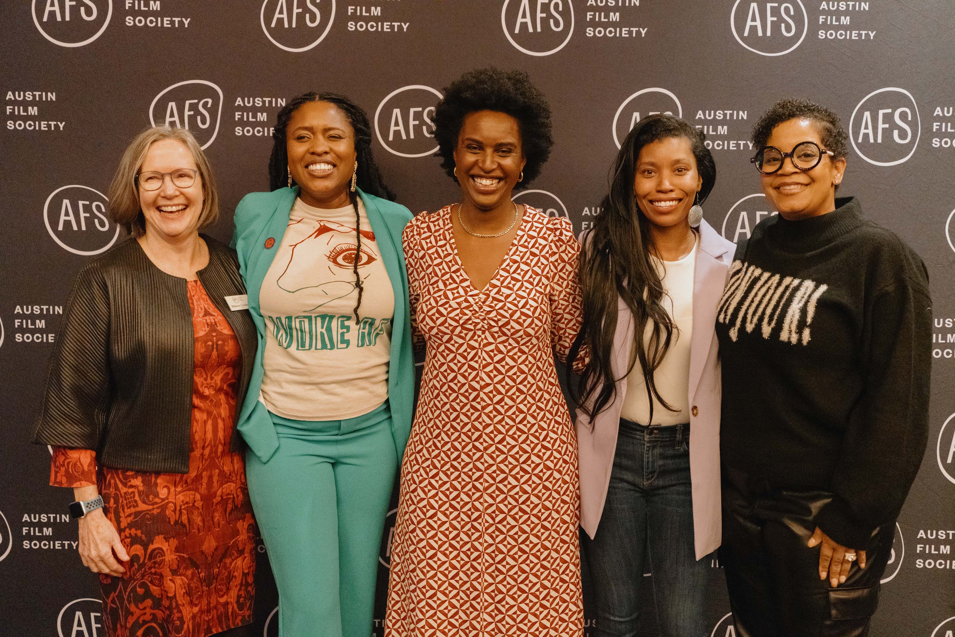 Five women standing together in front of a black backdrop with the Austin Film Society logo, smiling and posing for the photo.