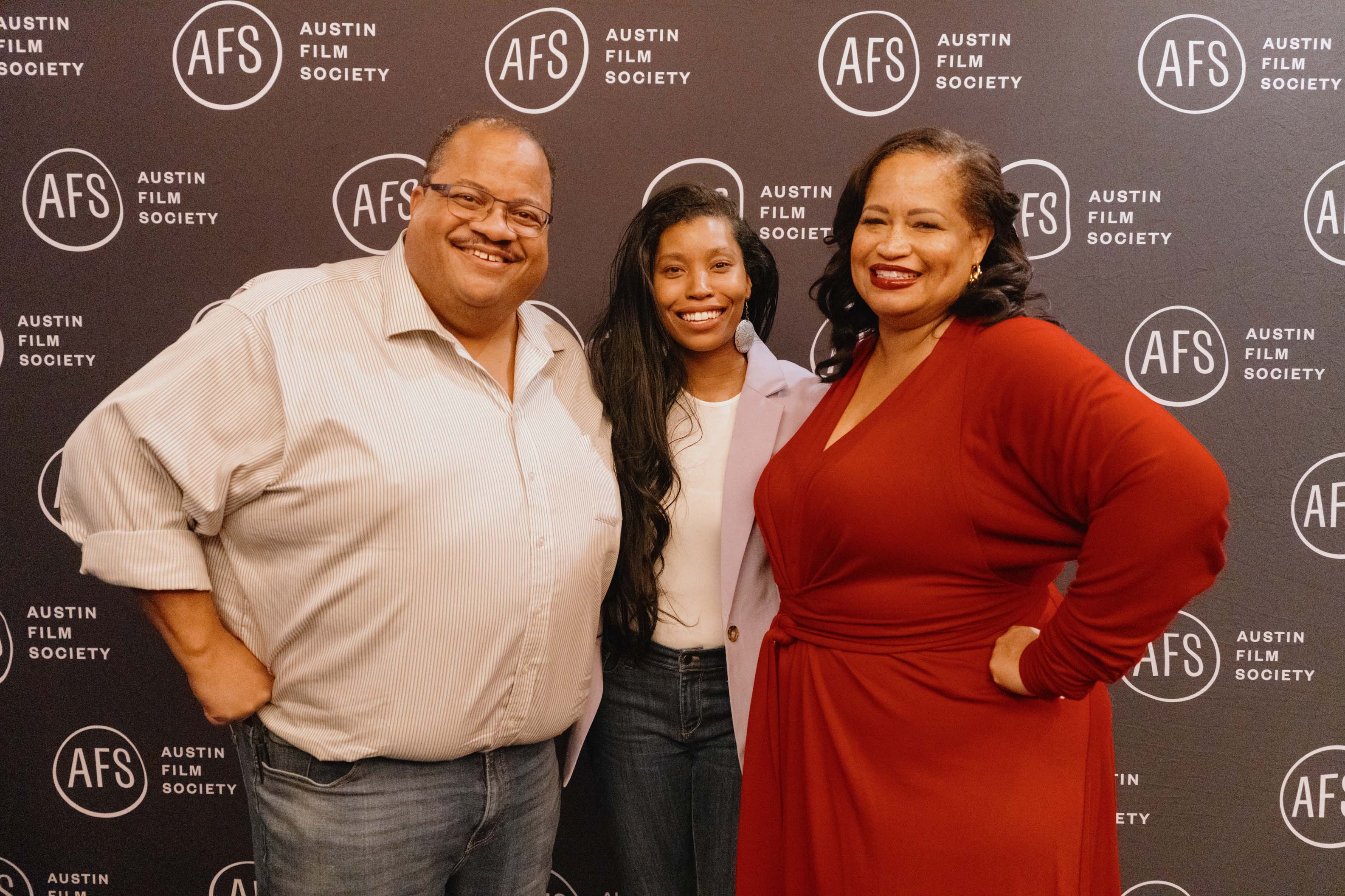 Three people smiling and posing in front of a backdrop with the Austin Film Society logo.