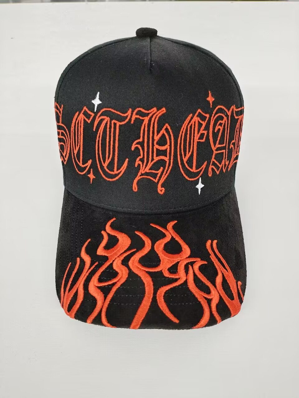 Black baseball cap with red stylized text and flame design, and small white star accents.