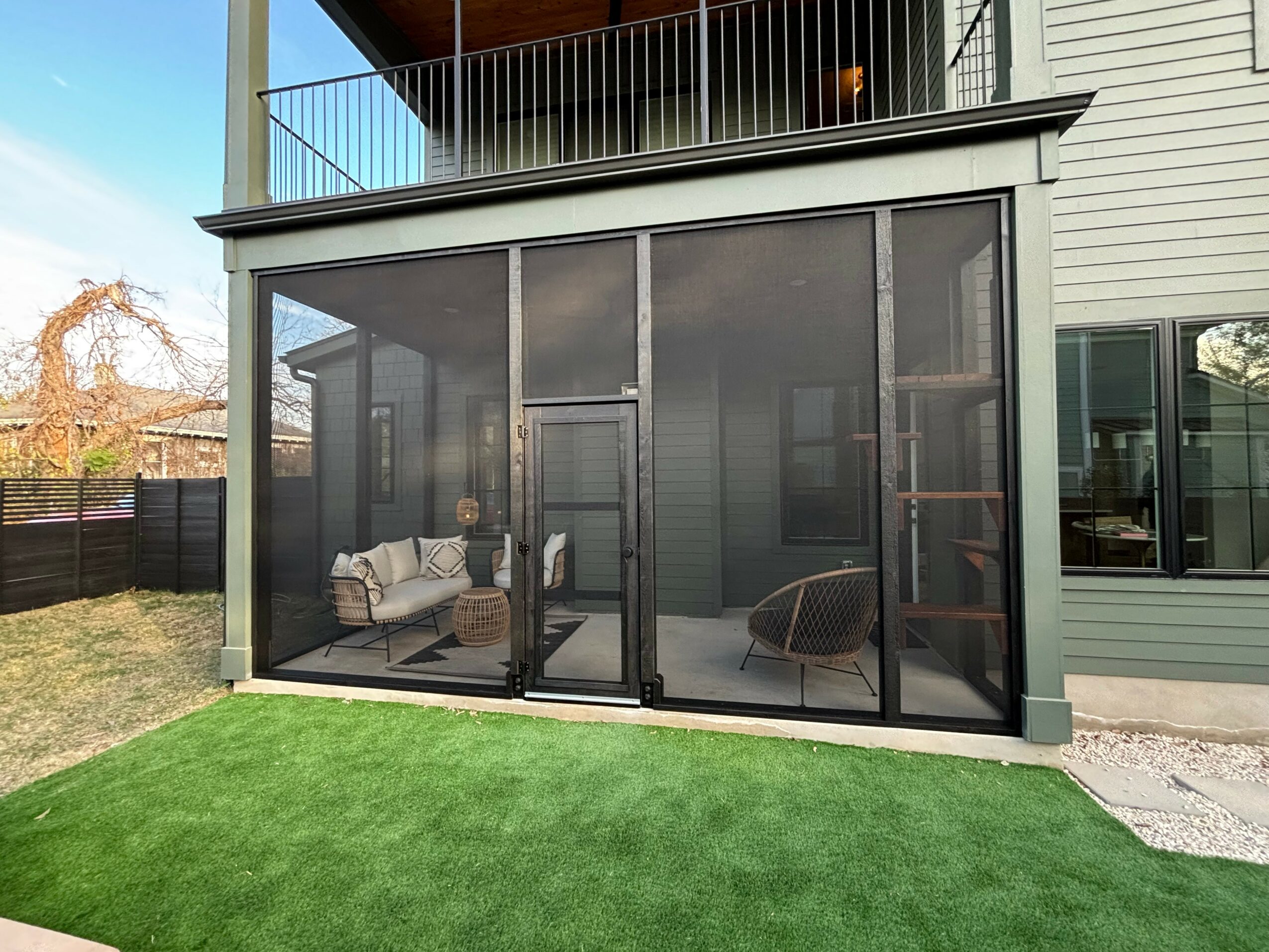 Enclosed porch with large glass sliding doors, outdoor furniture, and a green lawn in front.
