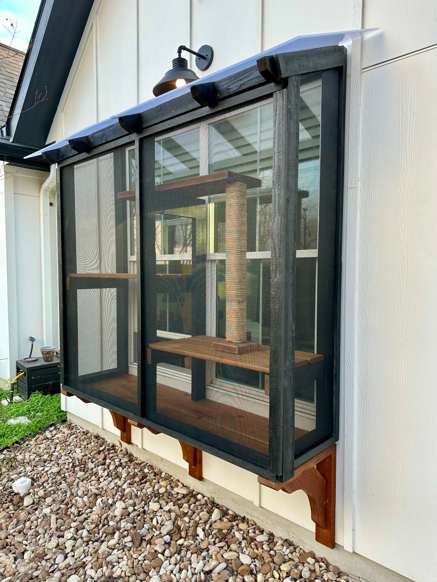 Enclosed outdoor cat porch with mesh walls, wooden platform, and a small door, attached to a house exterior.