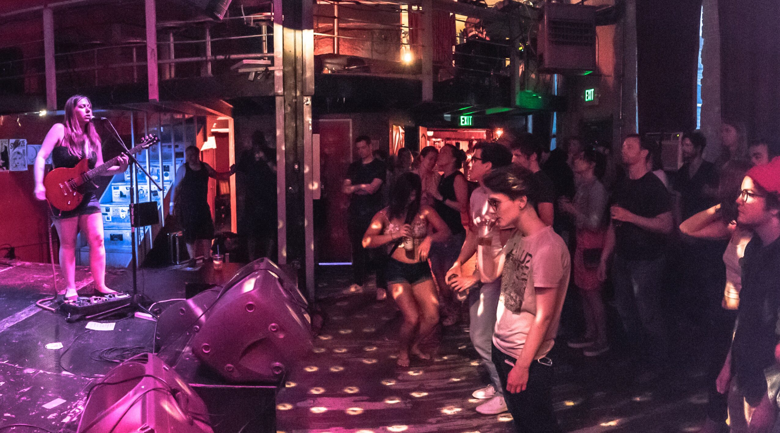 Musician performs on stage with audience dancing in a dimly lit venue.