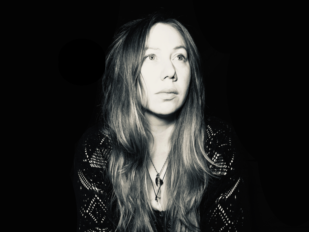 Black and white portrait of a woman with long hair, looking to the side, wearing a patterned top and necklace.