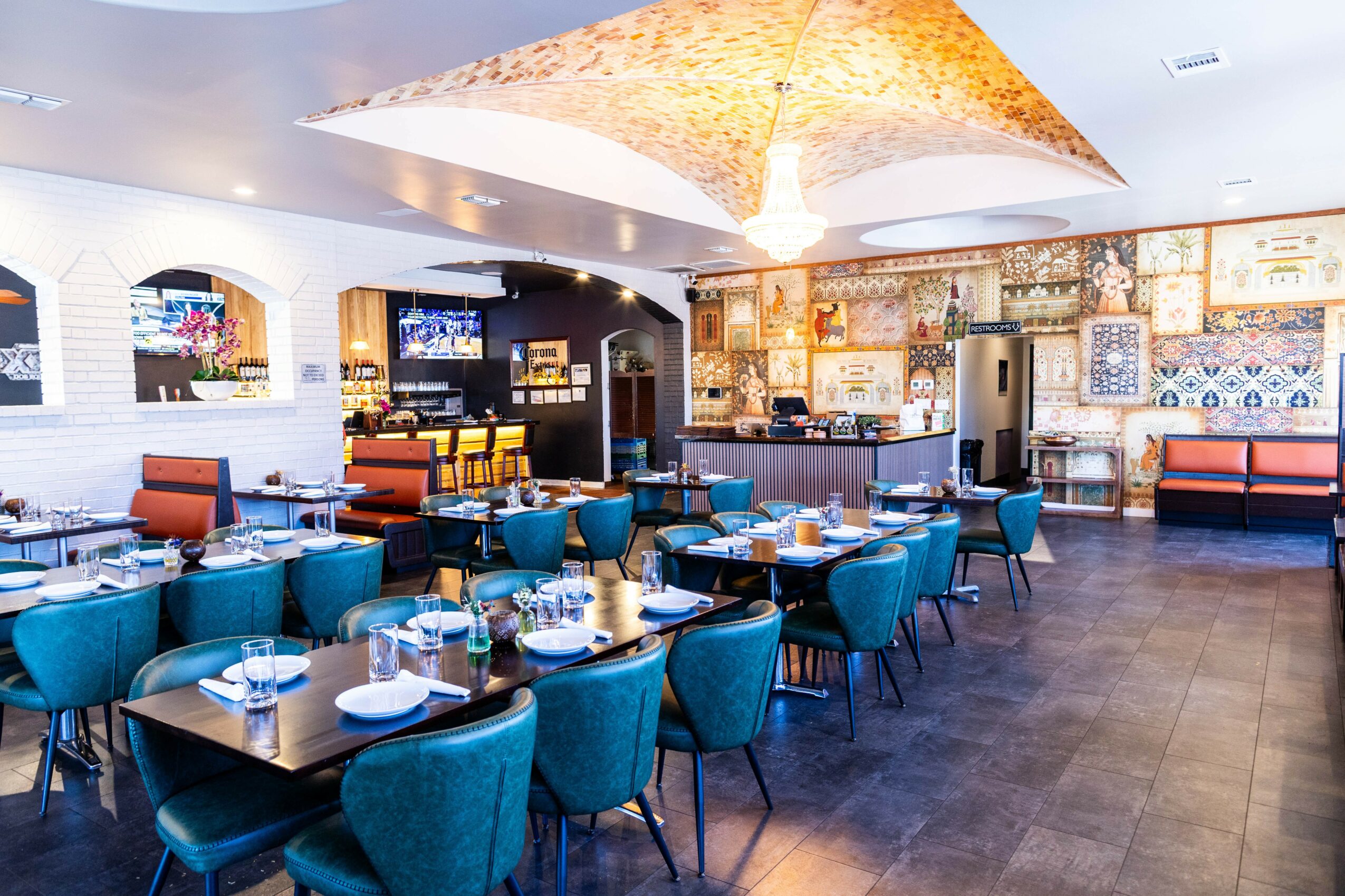 Restaurant interior with blue chairs, tables set with plates and glasses, and a decorative wall with patterned tiles.