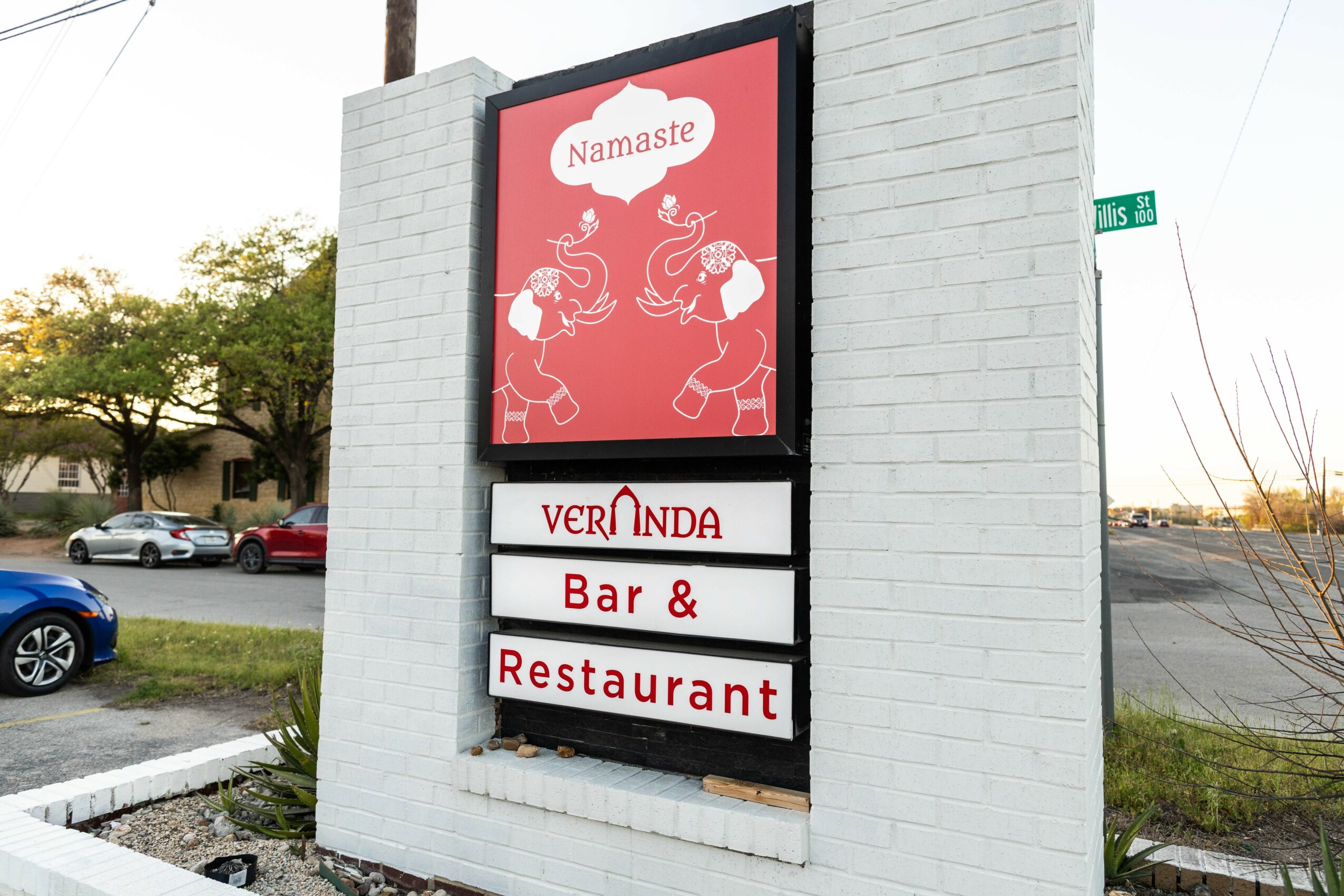 Signboard on a white brick wall with a red and white design, advertising a bar and restaurant named Veronda, with a Namaste message.