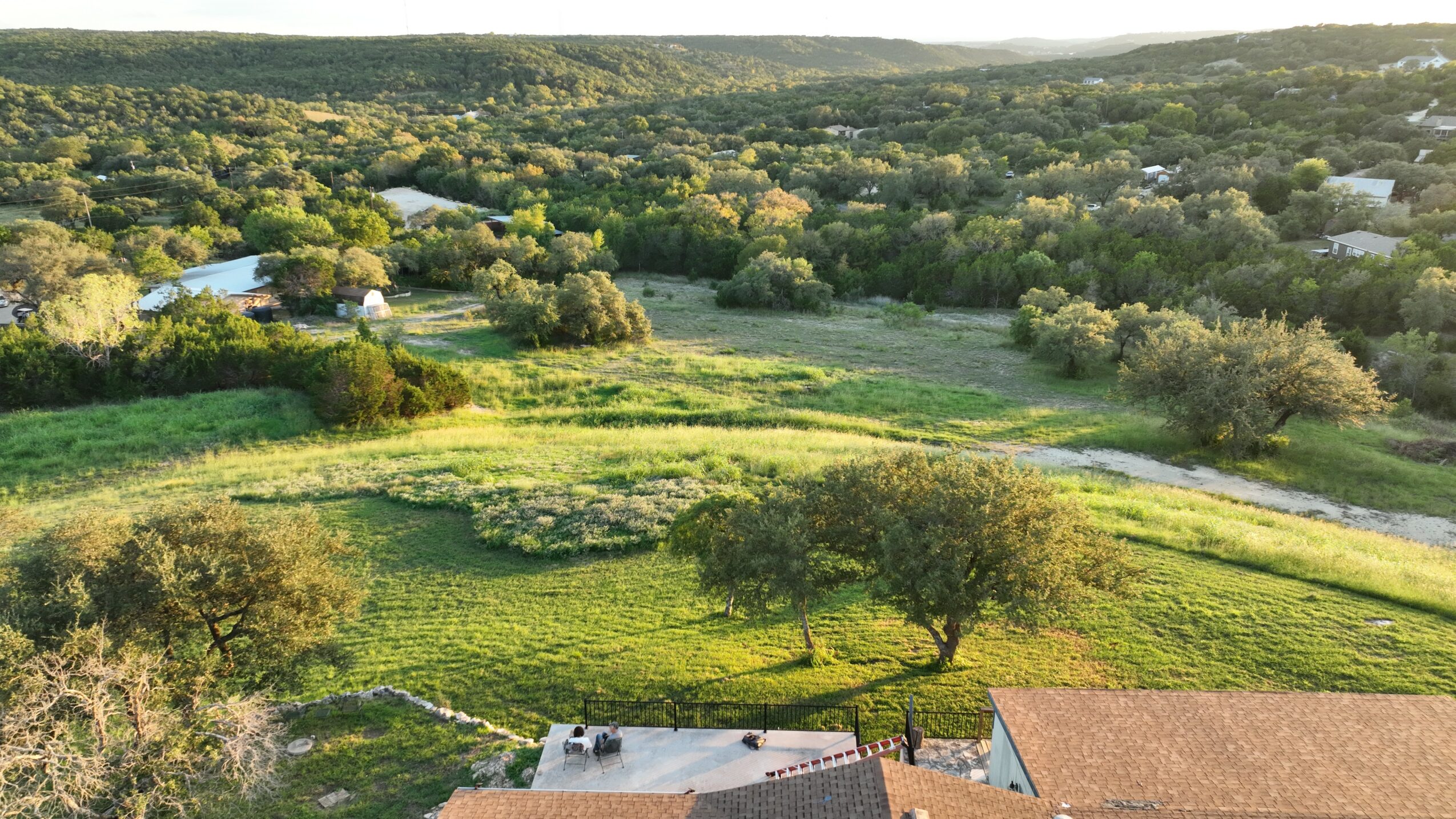 Landscape with green fields, trees, and a distant river, under a clear sky.