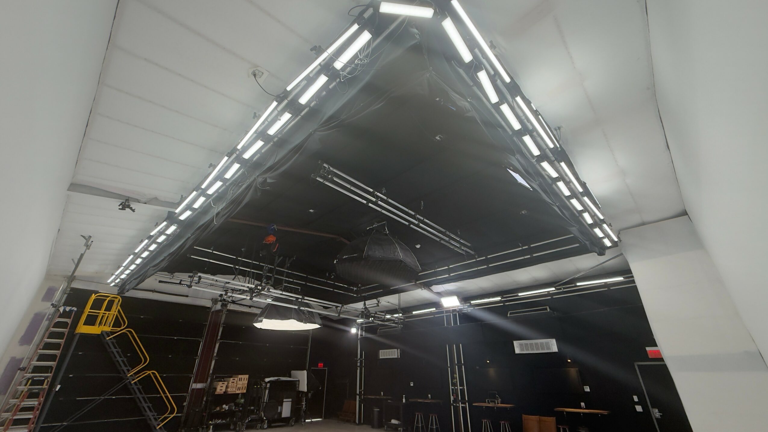 Ceiling with bright linear lights and dark central panel, with some equipment and structures visible below.