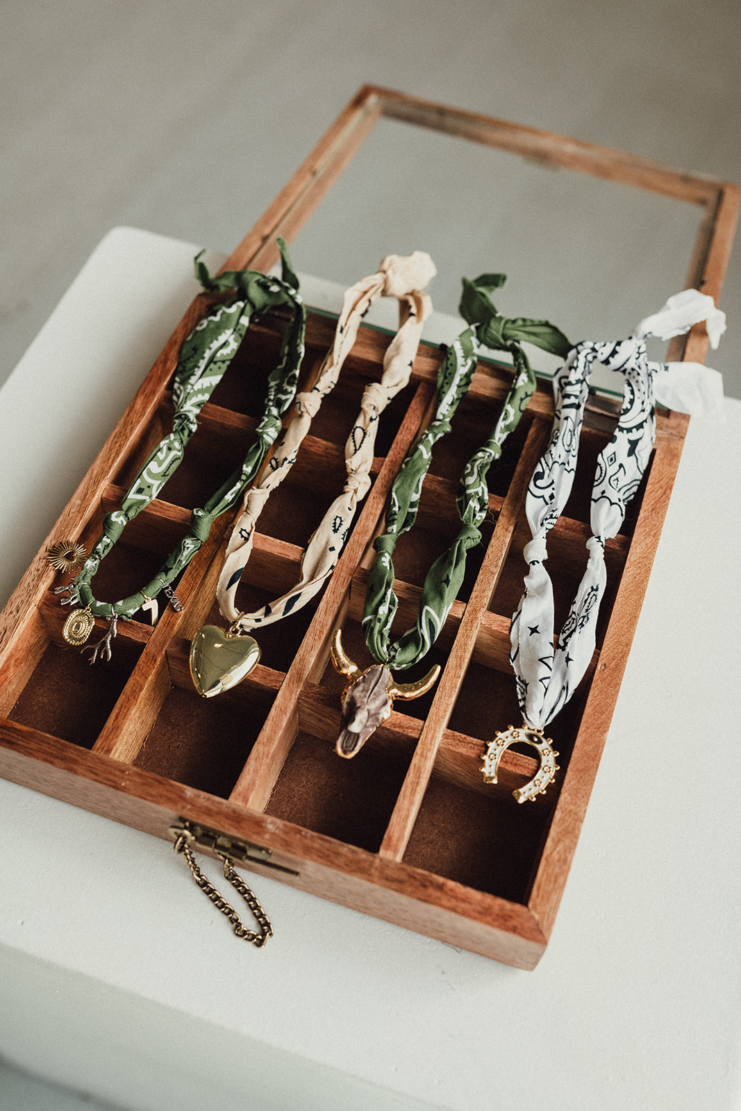 Four necklaces with patterned fabric and metal pendants in a wooden display box.