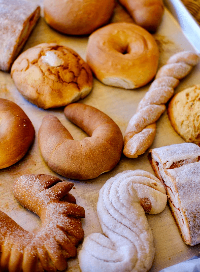 Assorted baked goods including bagels, cookies, bread, and pastries on a wooden surface.